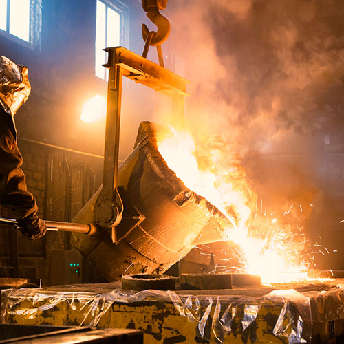 two smelter workers pouring a big bucket of molten metal into a cast